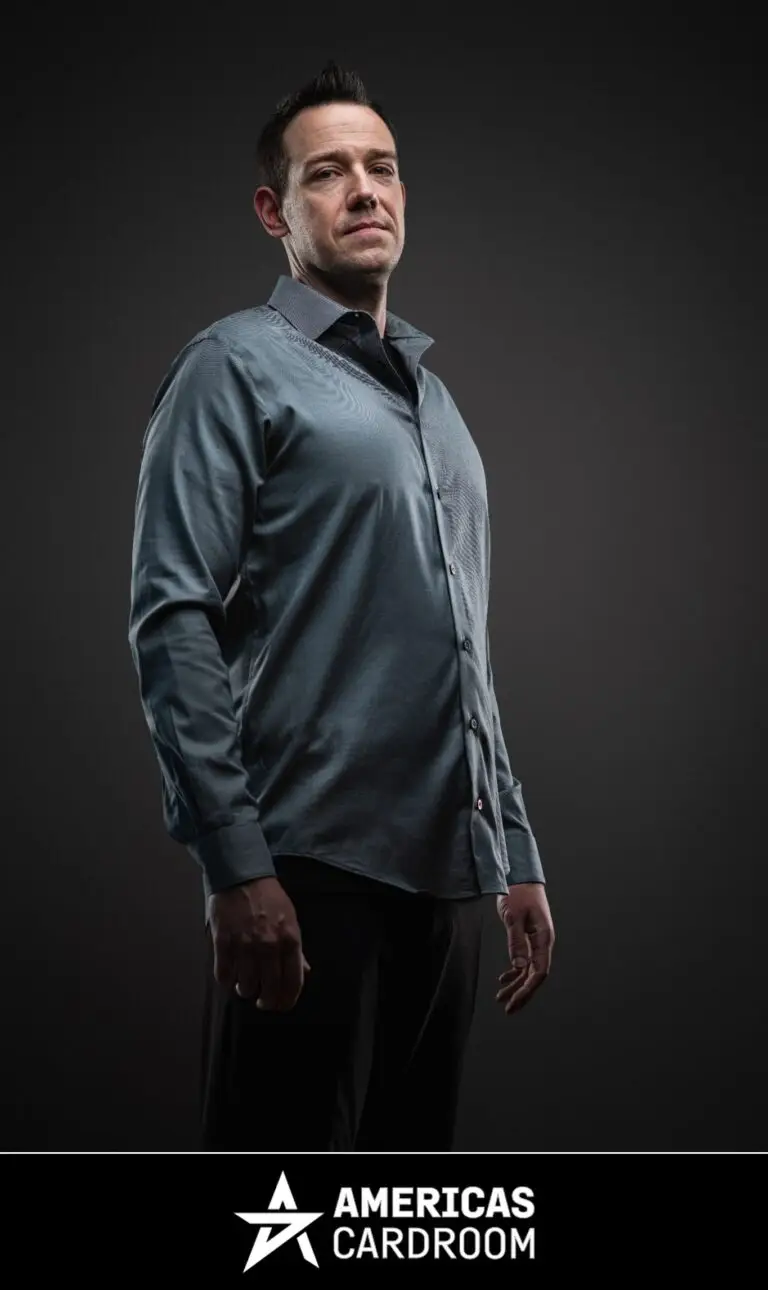 A medium shot of Jeff Boski, an ACR poker pro, looking directly at the camera with a serious expression. He is wearing a long-sleeved grey button-up shirt and black pants, against a dark background.