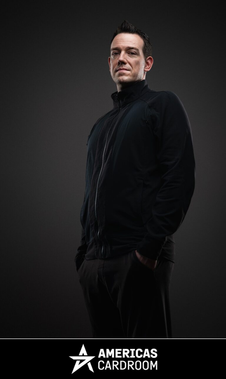 A medium shot of Jeff Boski, an ACR poker pro, looking directly at the camera with a serious expression. He is wearing a black zip-up jacket and black pants, with his hands in his pockets, against a dark background.
