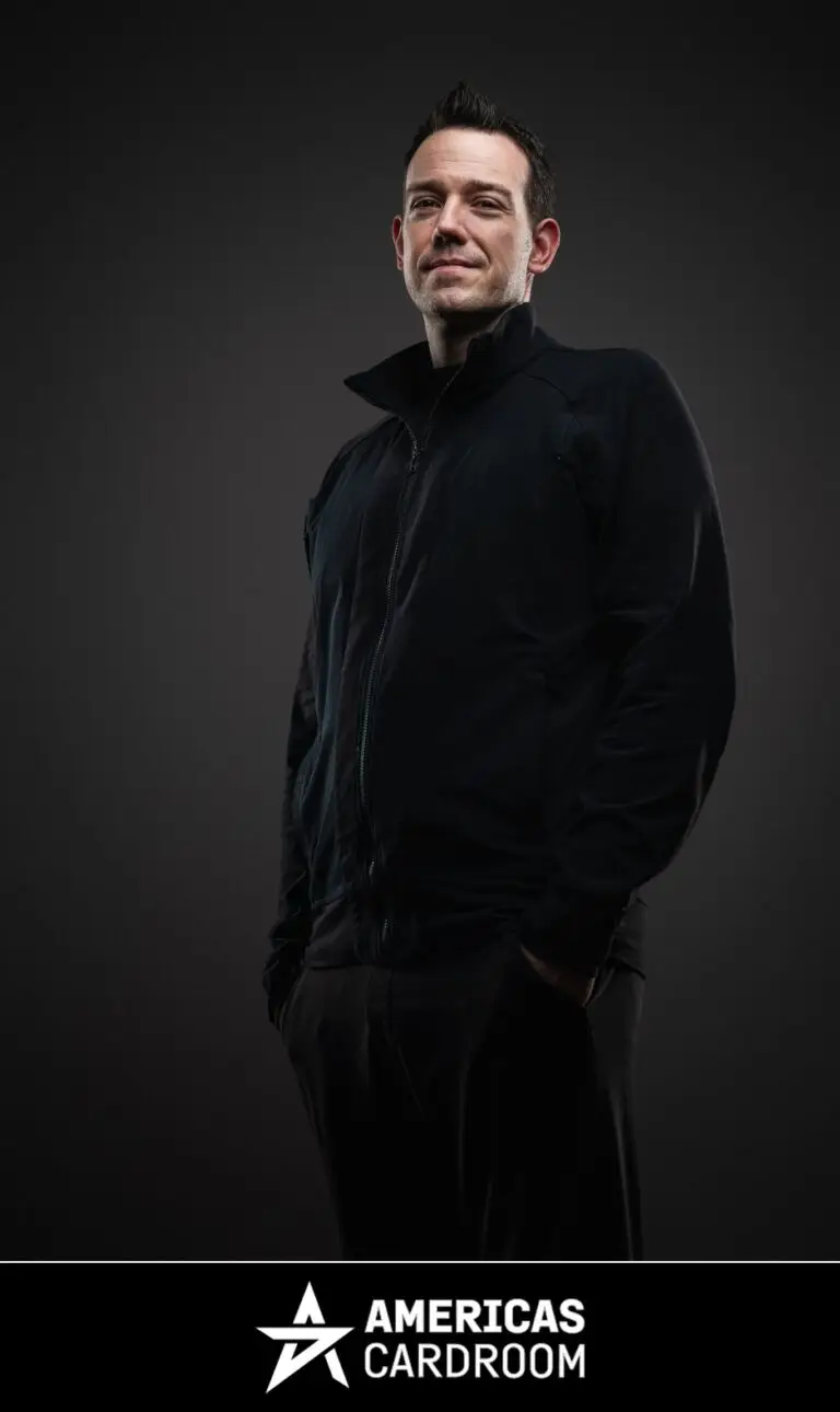 A medium shot of Jeff Boski, an ACR poker pro, looking up and to his left with a slight smile. He is wearing a black zip-up jacket and black pants, with his hands in his pockets, against a dark background.