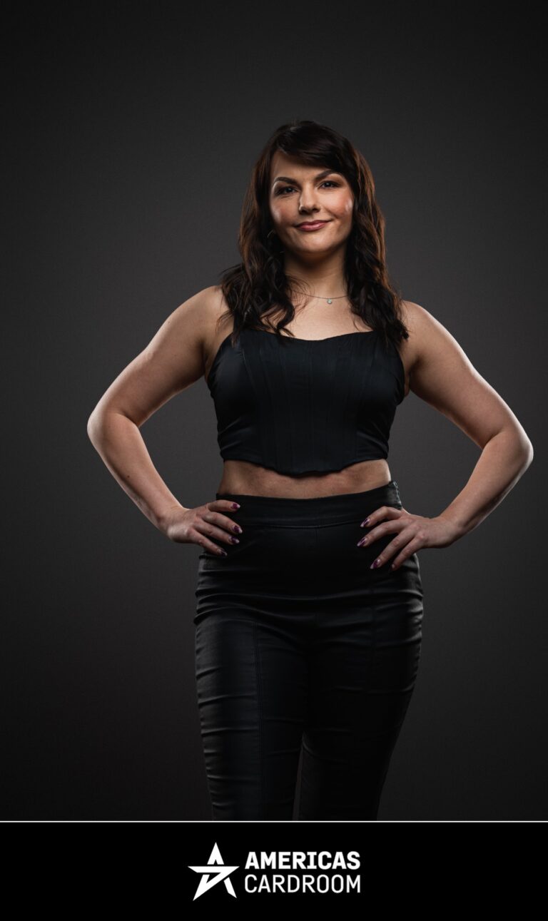 A full-body shot of Monika Zukowicz, an ACR poker pro, standing with her hands on her hips and a slight smile. She has dark, wavy hair and is wearing a black sleeveless crop top and black fitted pants, against a dark background.