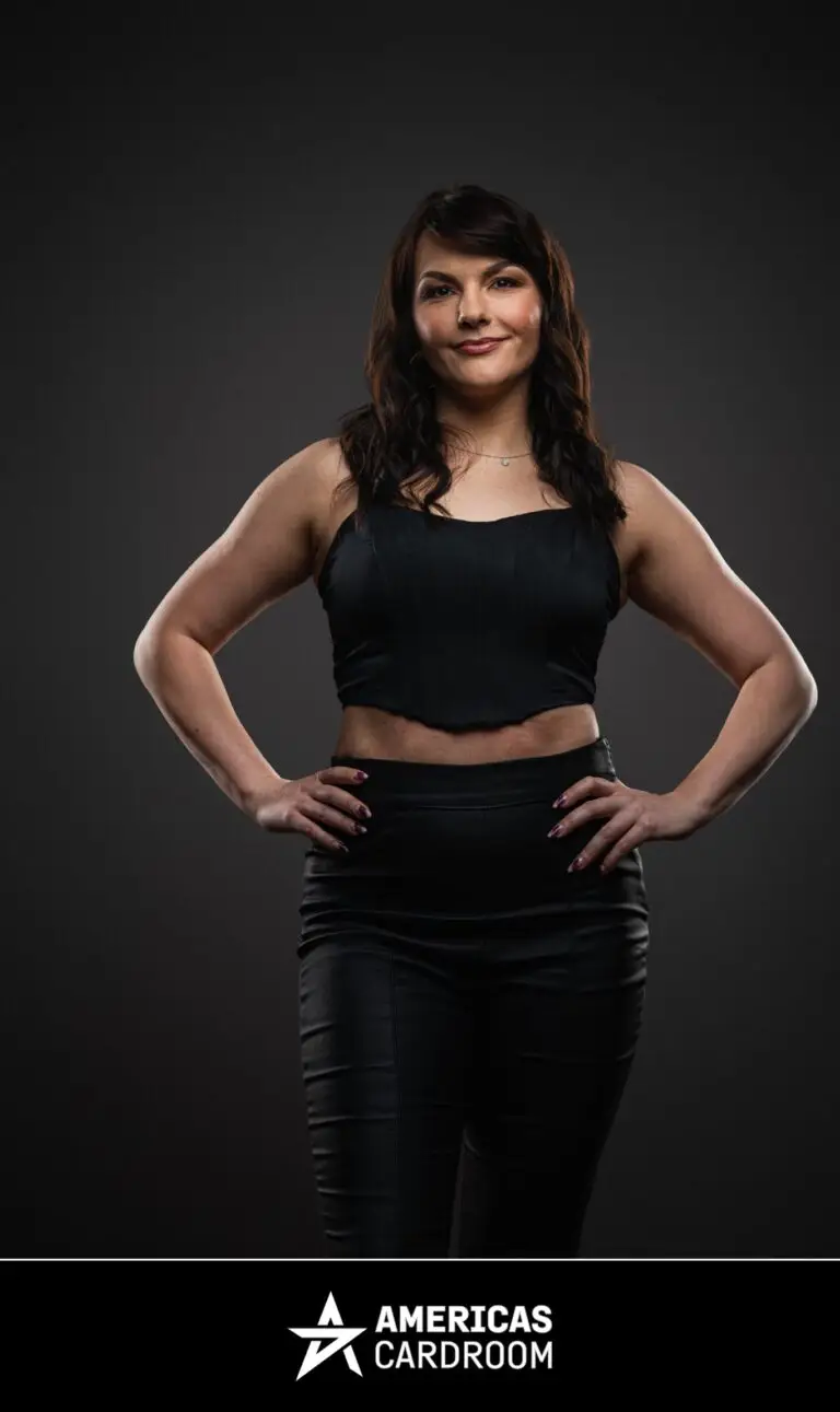 A full-body shot of Monika Zukowicz, an ACR poker pro, standing with her hands on her hips and a slight smile. She has dark, wavy hair and is wearing a black sleeveless crop top and black fitted pants, against a dark background.