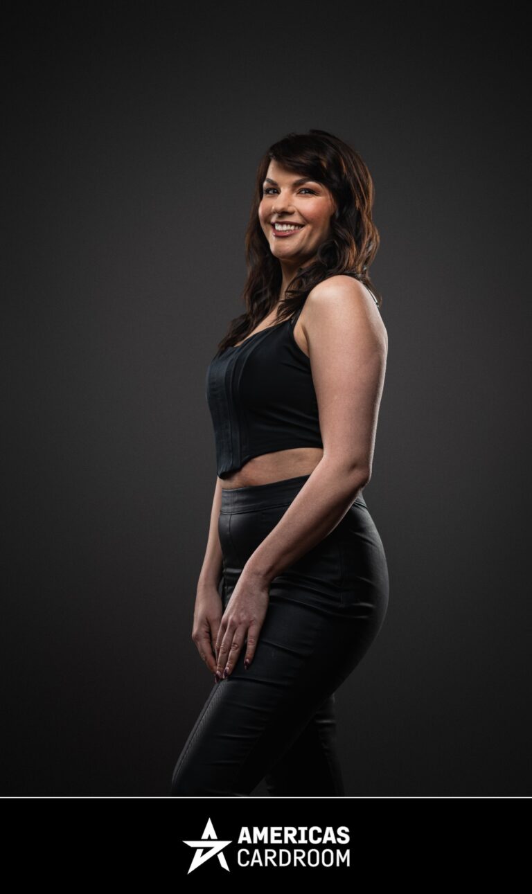 A three-quarter profile shot of Monika Zukowicz, an ACR poker pro, smiling and looking towards the camera. She has dark, wavy hair and is wearing a black sleeveless crop top and black fitted pants, against a dark background.