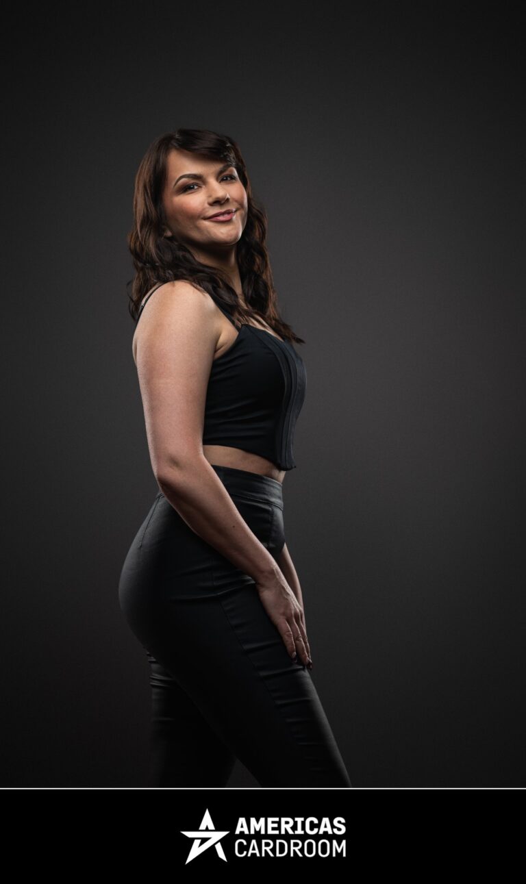 A three-quarter profile shot of Monika Zukowicz, an ACR poker pro, looking towards the camera with a slight smile. She has dark, wavy hair and is wearing a black sleeveless crop top and black fitted pants, against a dark background.
